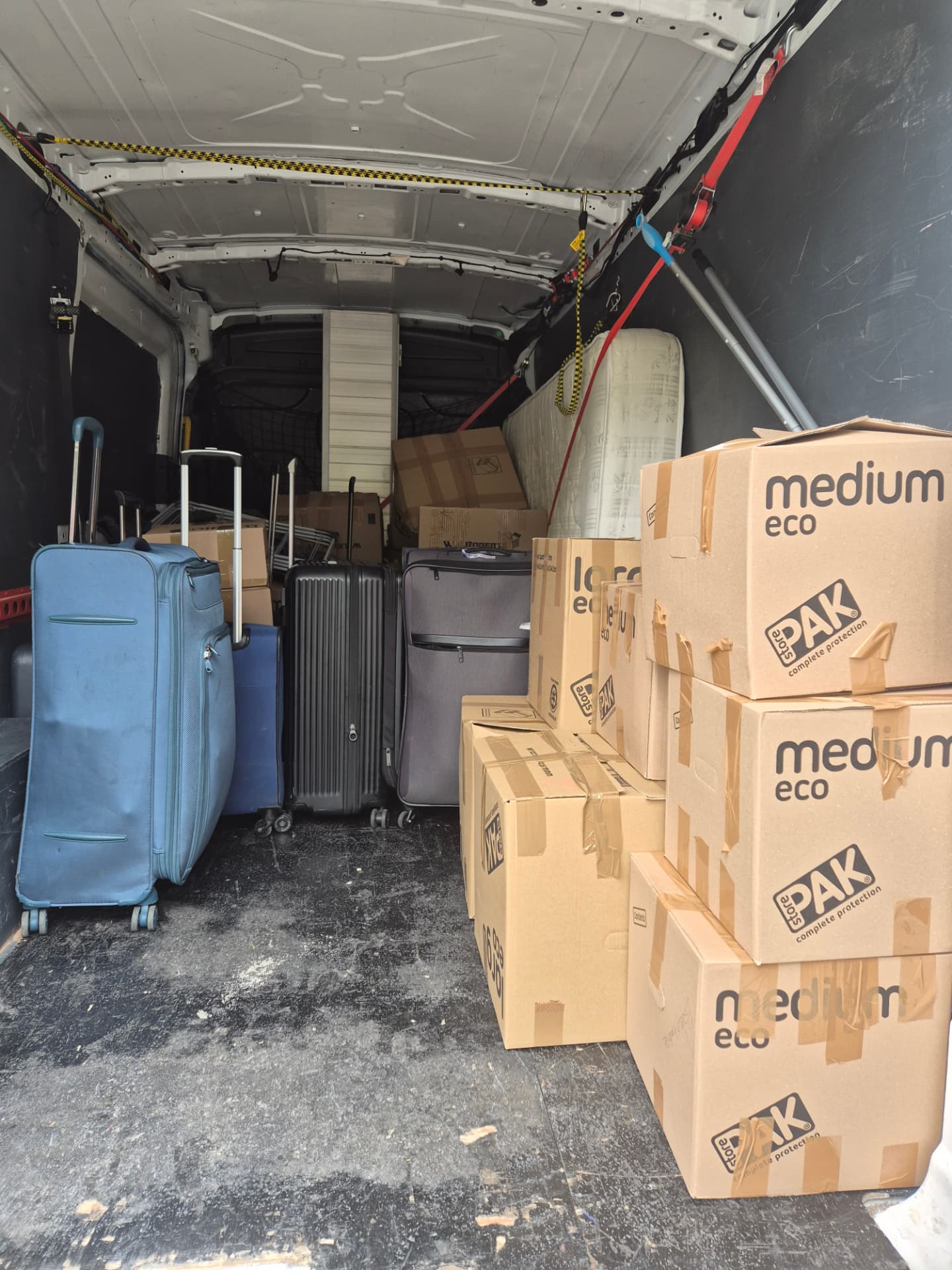 Suitcases, mattress and stacked moving boxes loaded into a Ford Transit LWB van on a flat move