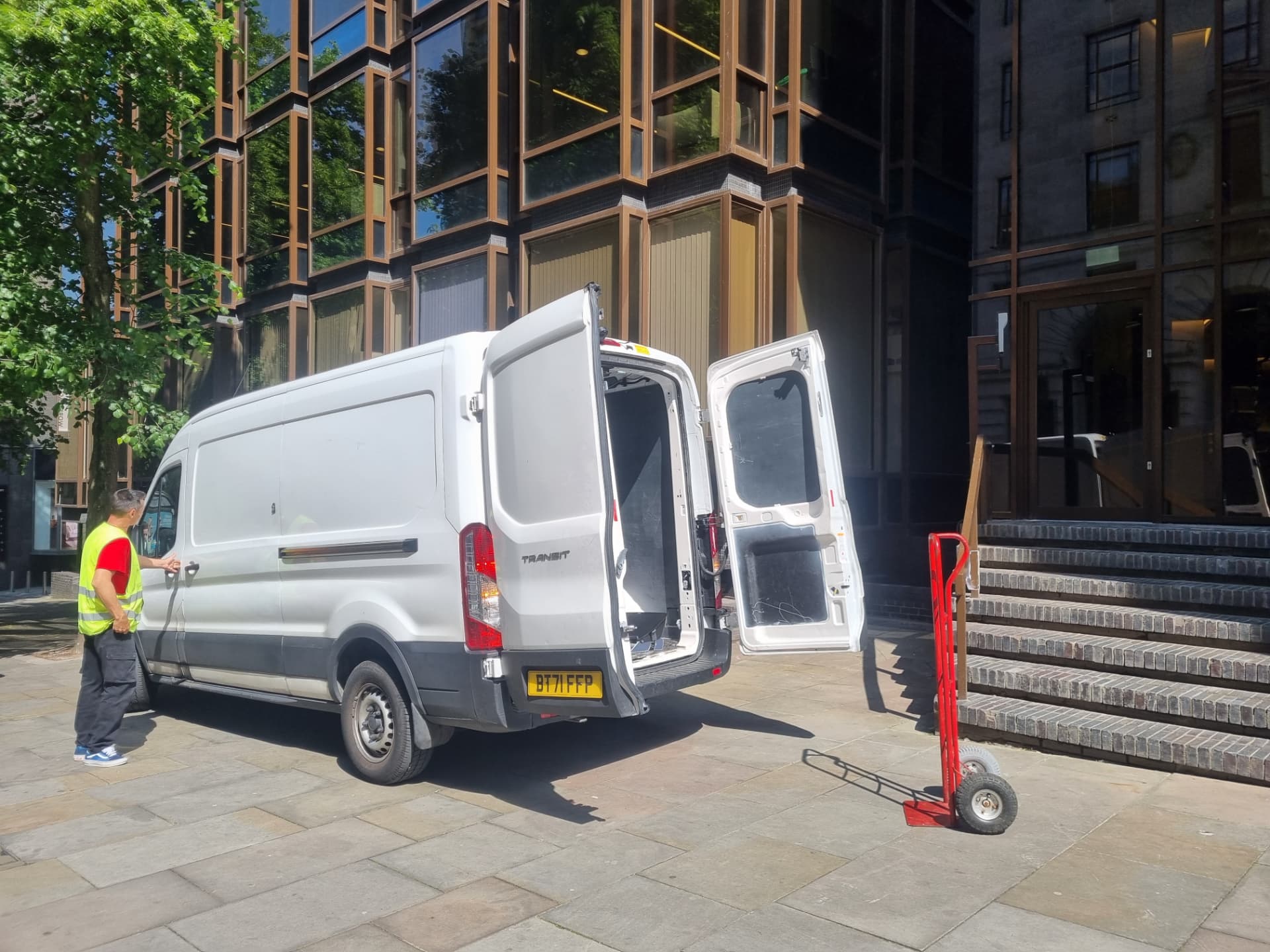Ford Transit LWB 15m³ van with rear doors open and a sack truck ready outside a Manchester city centre office building